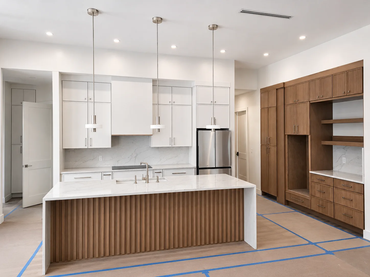 Finished Sarasota kitchen replacement with island, white cabinetry, wood storage wall, countertops, and pendant lights