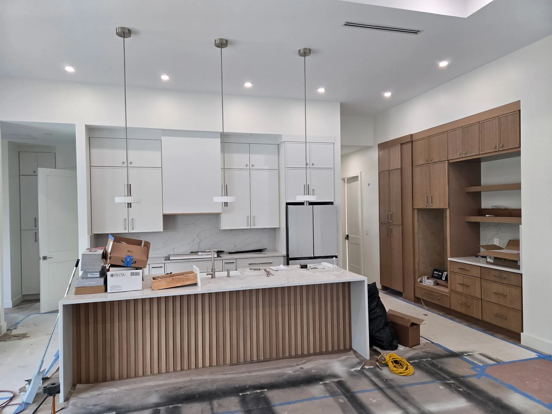 Sarasota two-tone kitchen replacement in progress with island, white cabinets, wood storage cabinetry, and pendant lighting