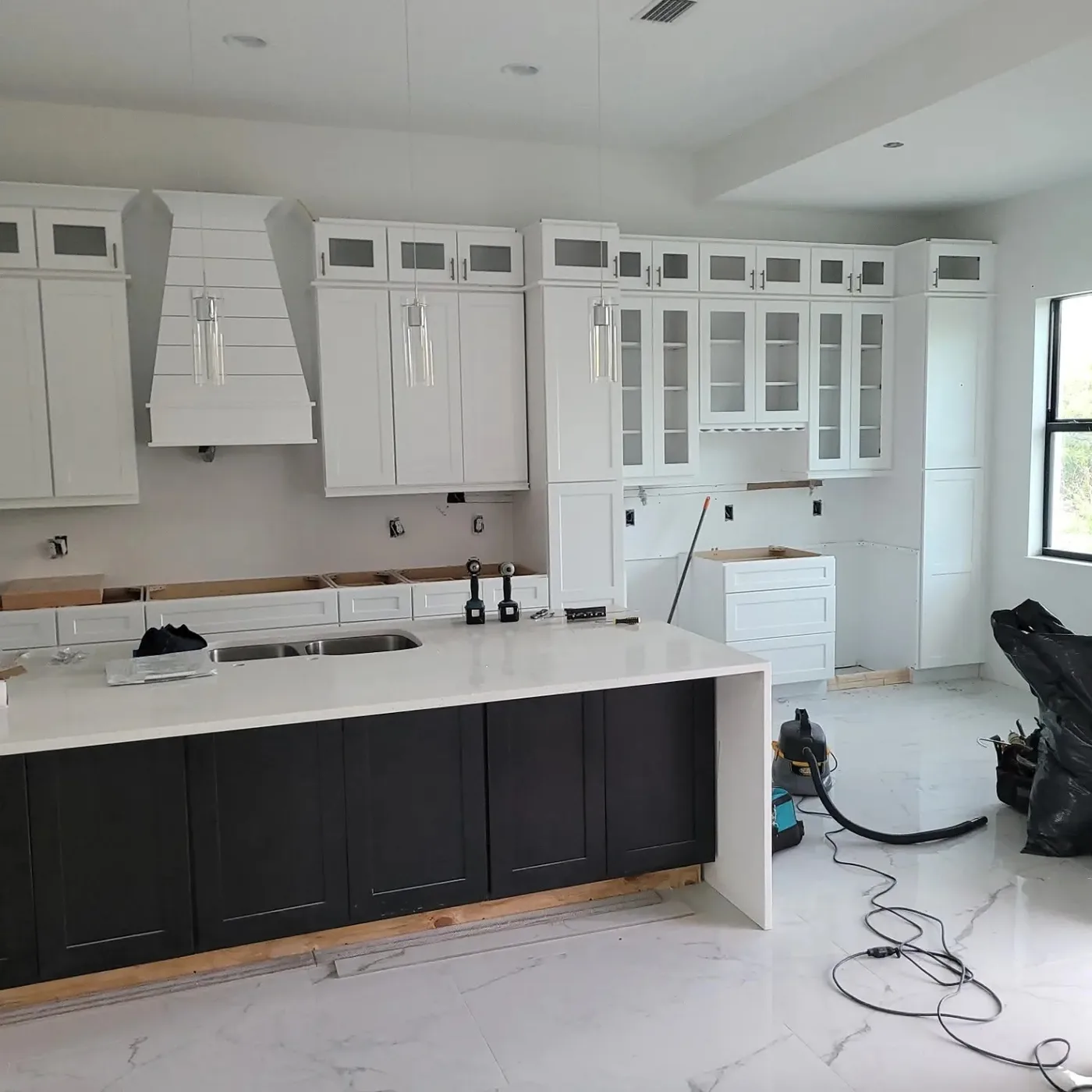 Venice-area kitchen remodel progress with white wall cabinets, black island cabinets, countertop, and open finish work